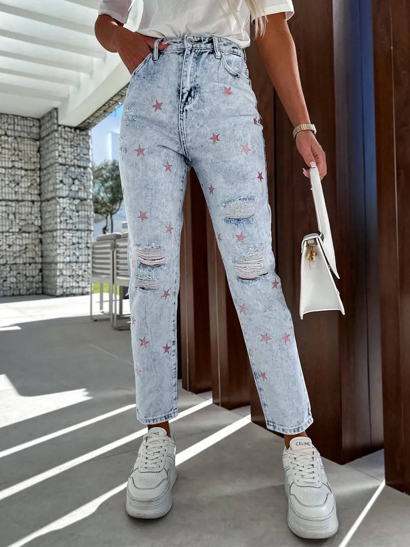 Person wearing light blue jeans with star patterns, white sneakers, and a white handbag outdoors.