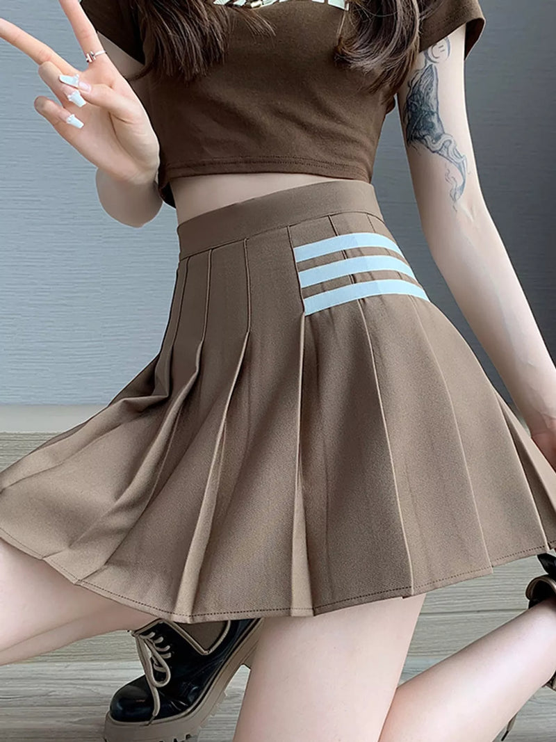A person wearing a brown pleated mini skirt with three light blue horizontal stripes near the waistband, paired with a matching brown crop top and black platform shoes.