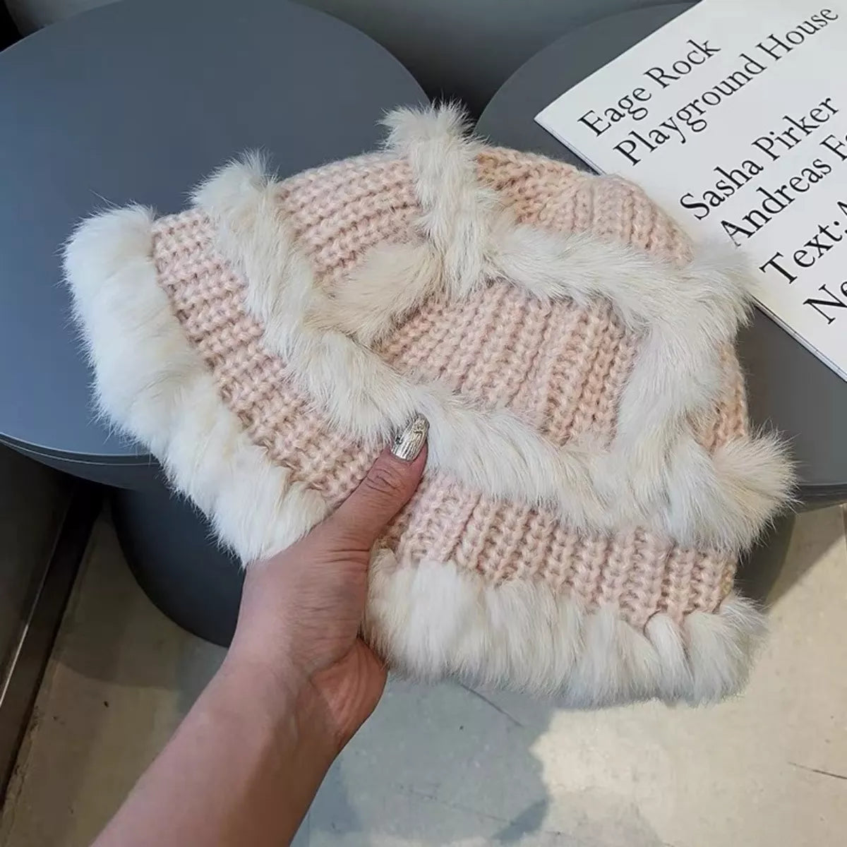 Pink knitted hat with white fur trim held by a hand on a blurred background