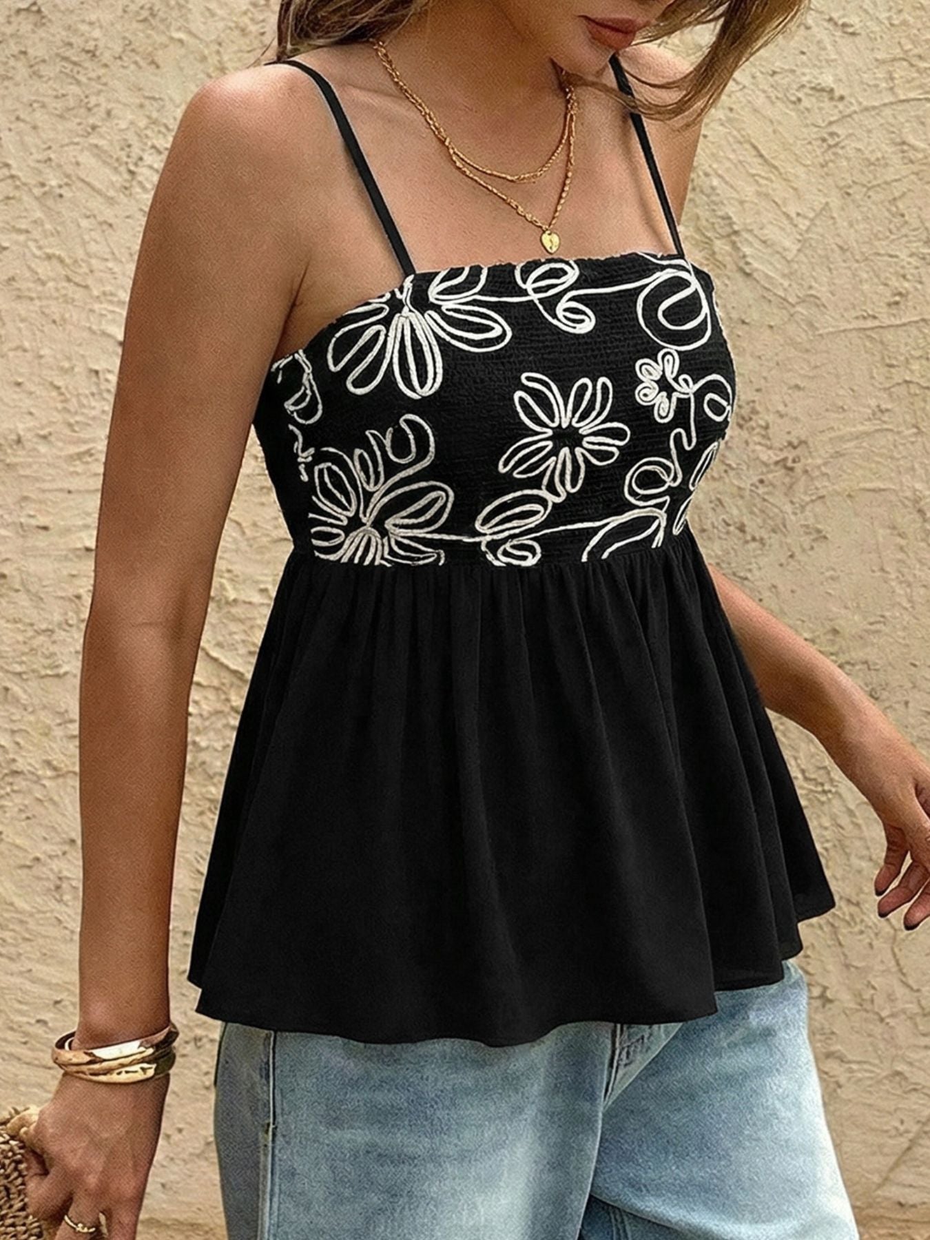 Black floral-patterned top worn by a person against a beige wall.