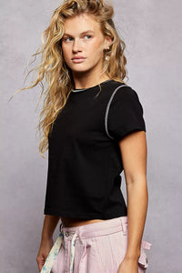 Woman wearing a black t-shirt and pink pants against a gray background