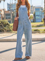 Woman wearing a denim jumpsuit holding a drink on a street.