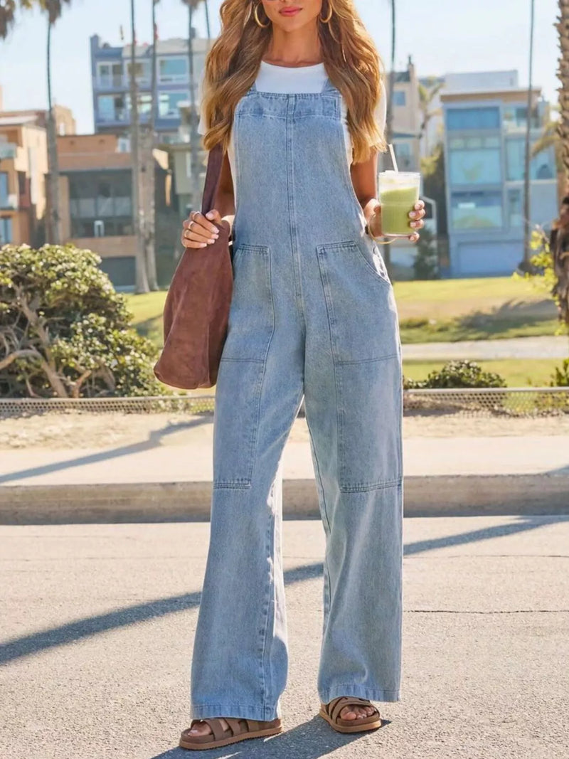 Woman wearing a denim jumpsuit holding a drink on a street.