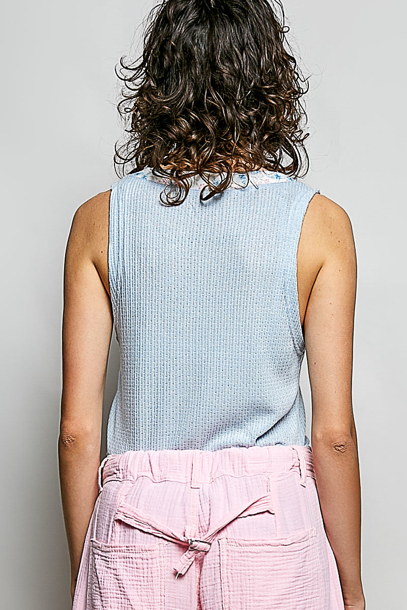Person wearing a light blue sleeveless top and pink pants on a gray background