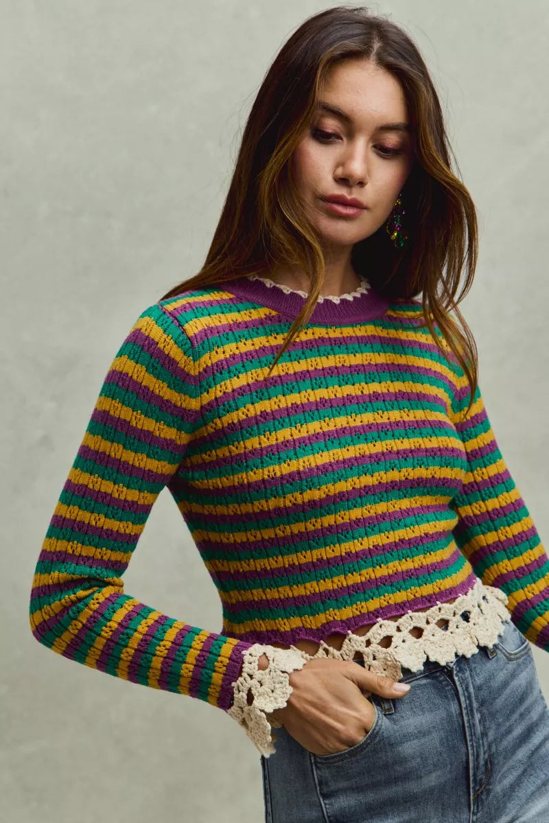 Woman wearing a colorful striped sweater with lace trim against a neutral background