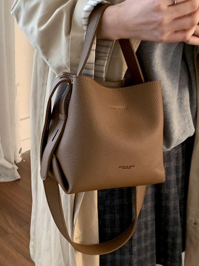 Brown leather handbag held by a person wearing a light-colored coat.