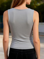 Person wearing a light gray sleeveless top with a blurred outdoor background