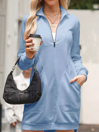 Woman wearing a blue dress with a zipper, holding a black handbag and a white cup.