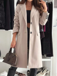 Person wearing a long beige coat holding a handbag in a clothing store.