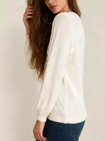 Woman wearing a white sweater with a subtle pattern on a plain background