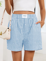 Person wearing blue and white checkered shorts with a beige handbag on a light background