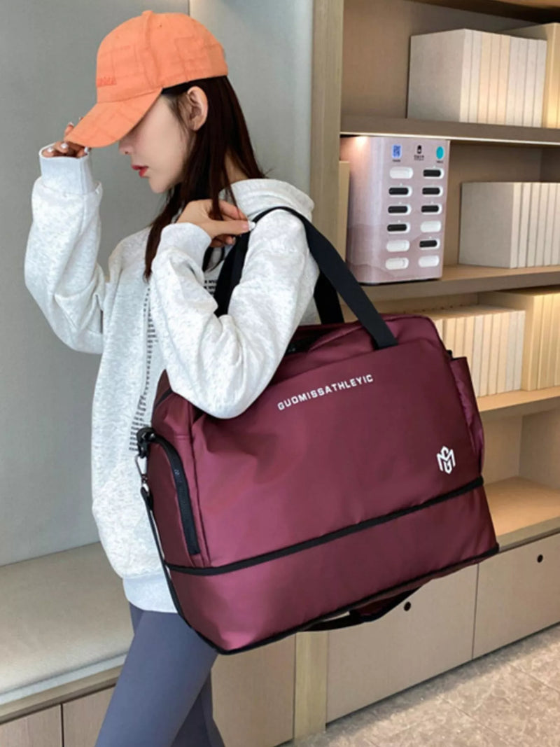 Person holding a maroon duffel bag with a visible brand logo in an indoor setting.