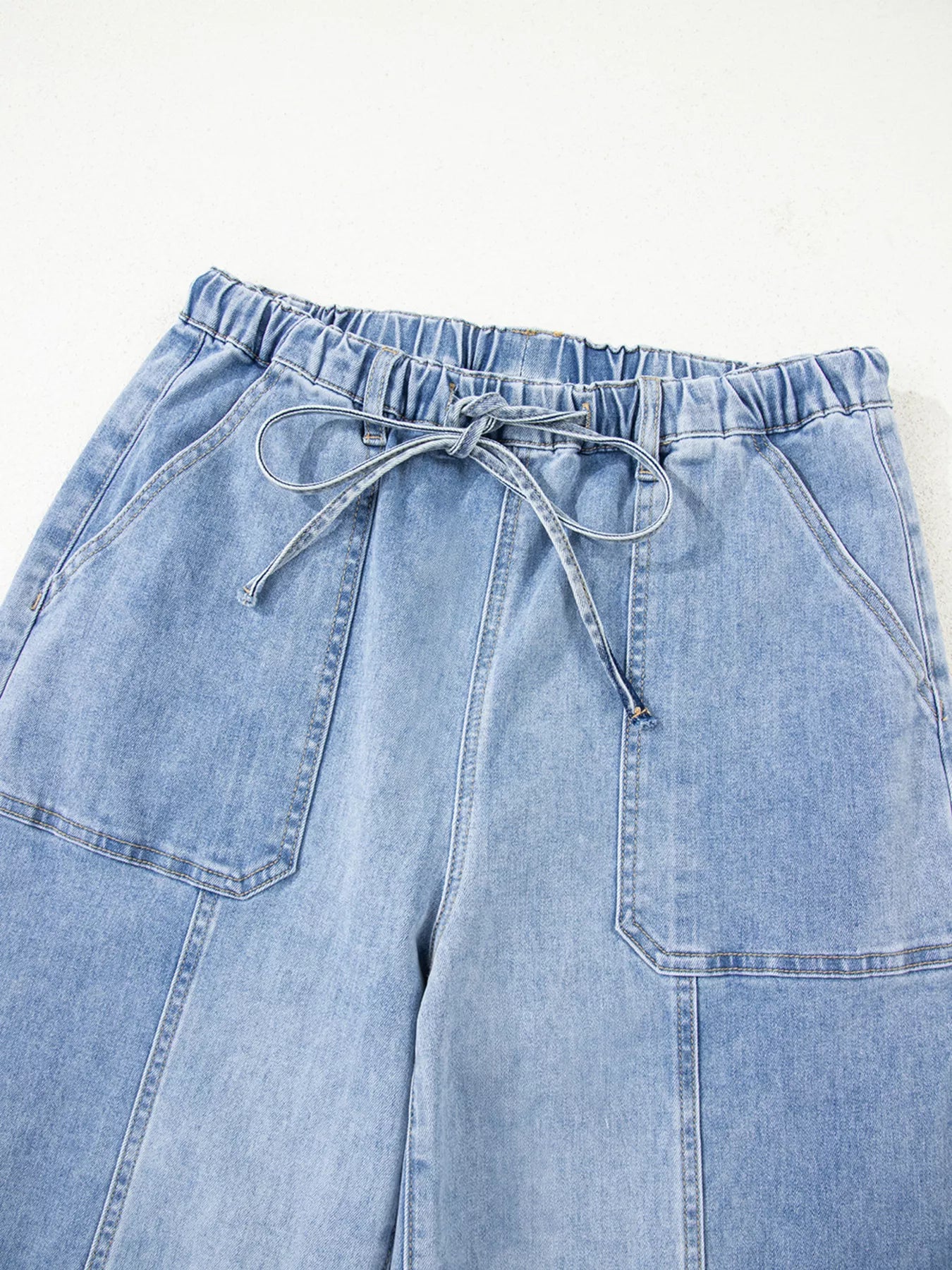 Light blue denim pants with a drawstring waist on a white background