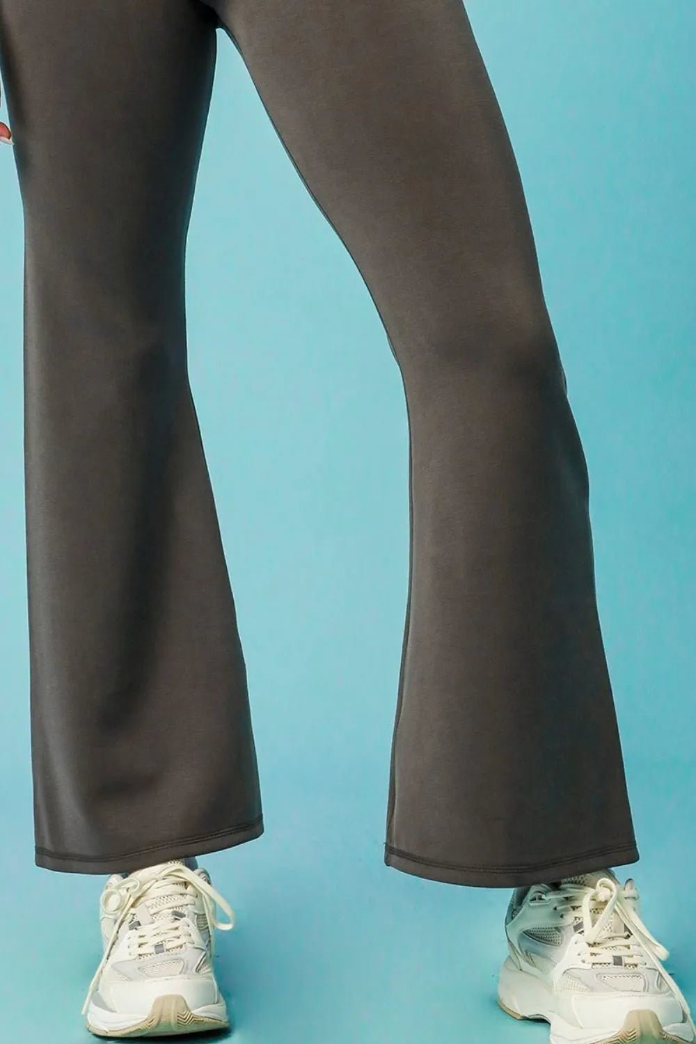 Dark brown flared pants worn with white sneakers on a light blue background