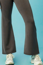 Dark brown flared pants worn with white sneakers on a light blue background