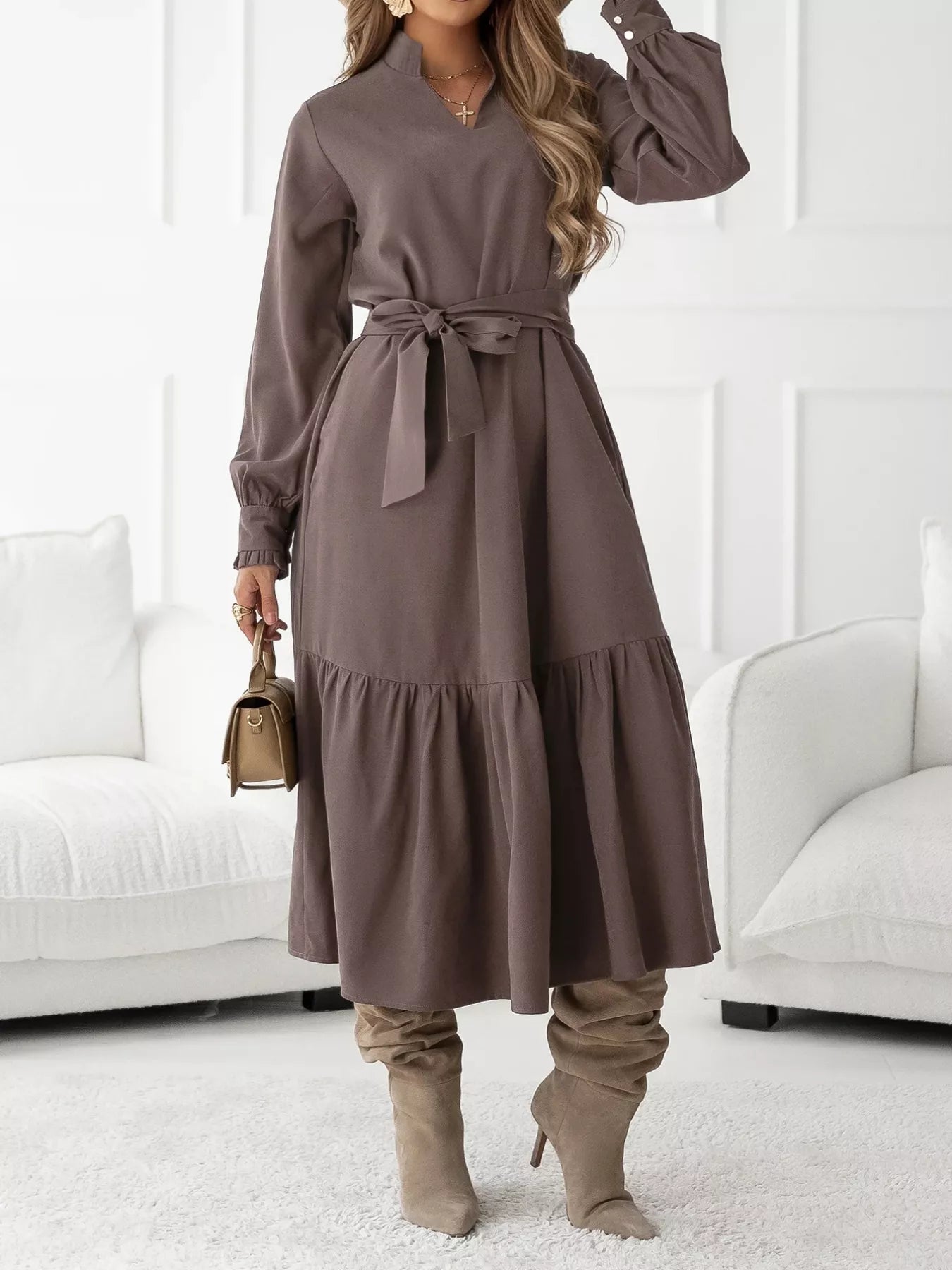 Woman wearing a brown dress with long sleeves and a belt, standing in a room with white furniture.