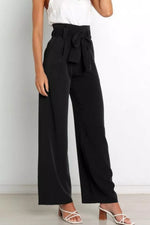 Person wearing black wide-leg pants with a white top on a plain background