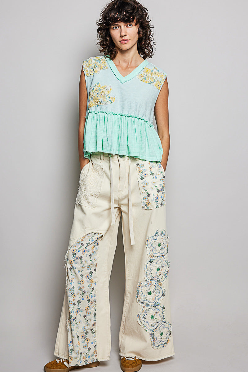 Woman wearing a light green top and cream pants with floral patterns against a gray background