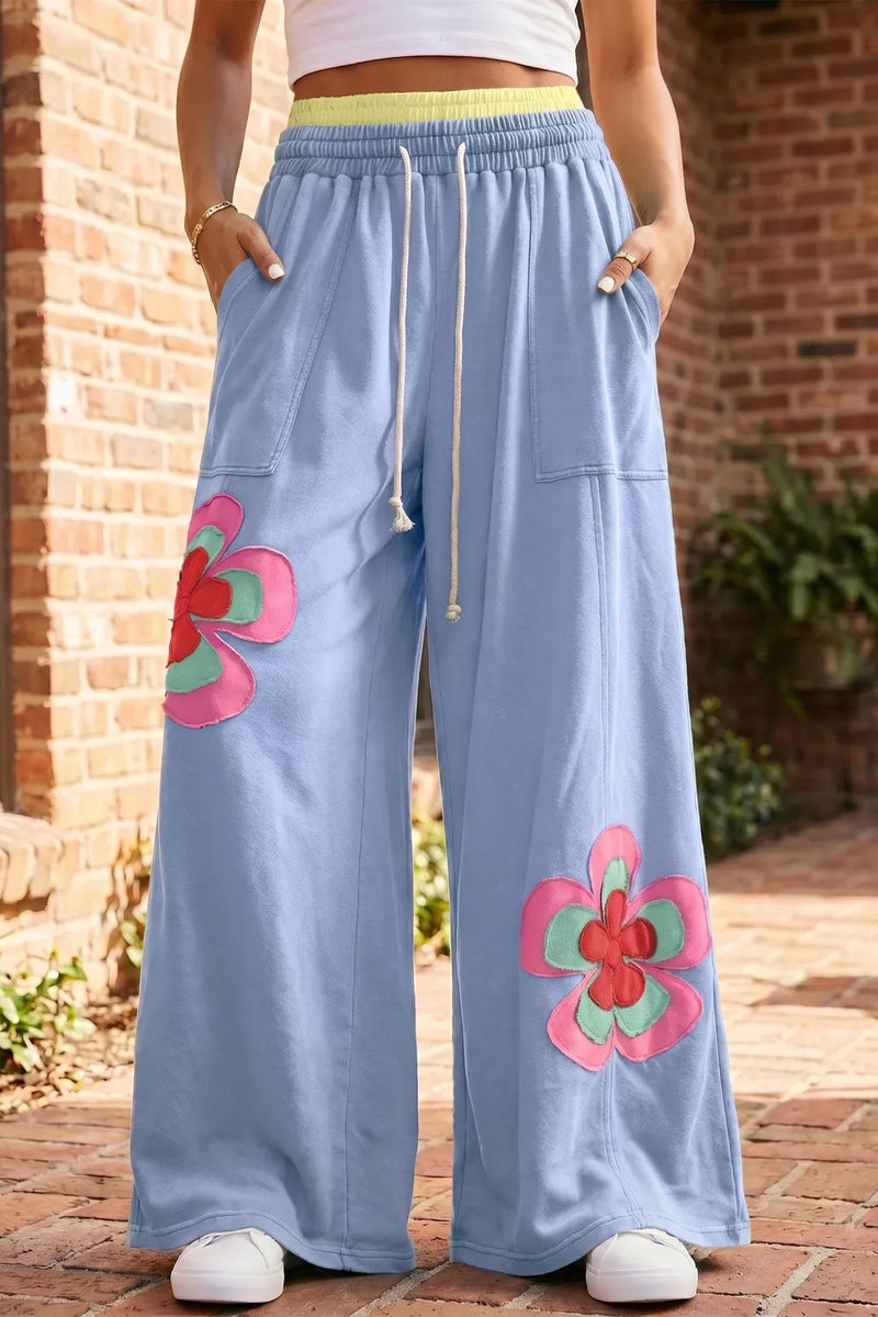 Light blue pants with pink floral designs worn by a person in front of a brick wall.