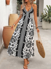 Woman wearing a black and white patterned dress holding a straw bag outdoors.