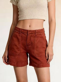 Person wearing rust-colored shorts and a beige top on a plain background