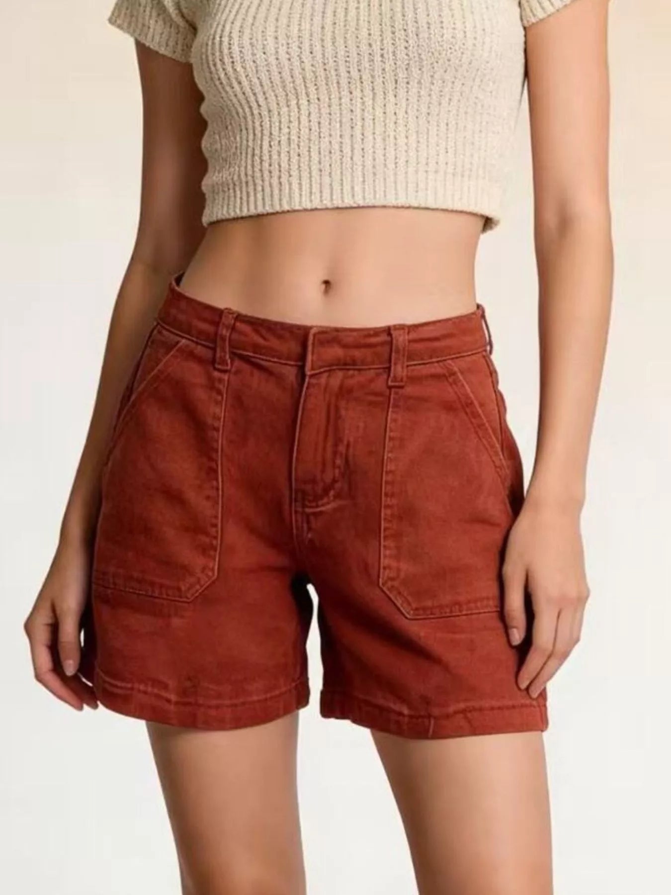 Person wearing rust-colored shorts and a beige top on a plain background