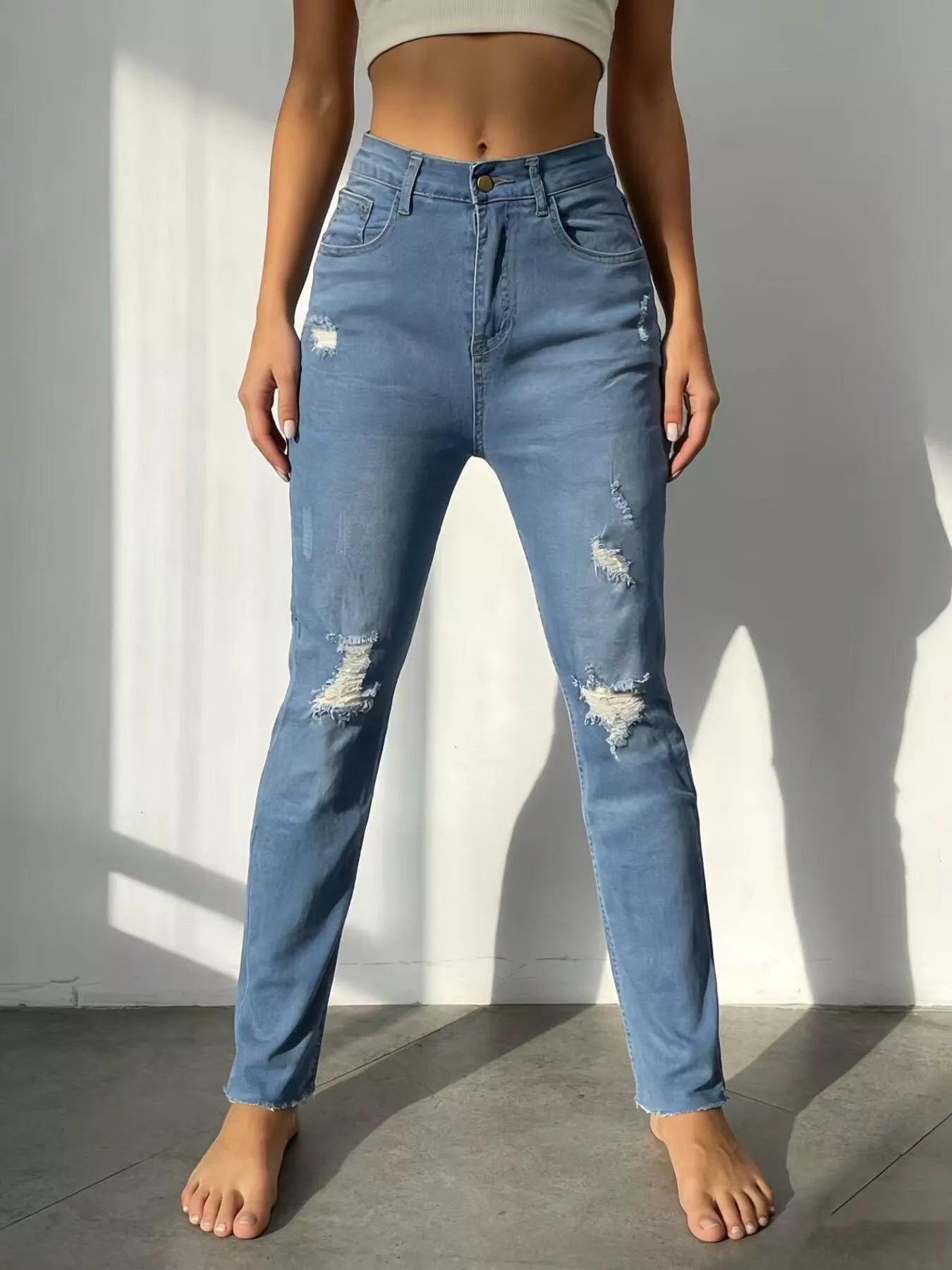 Person wearing blue distressed jeans standing against a plain wall.