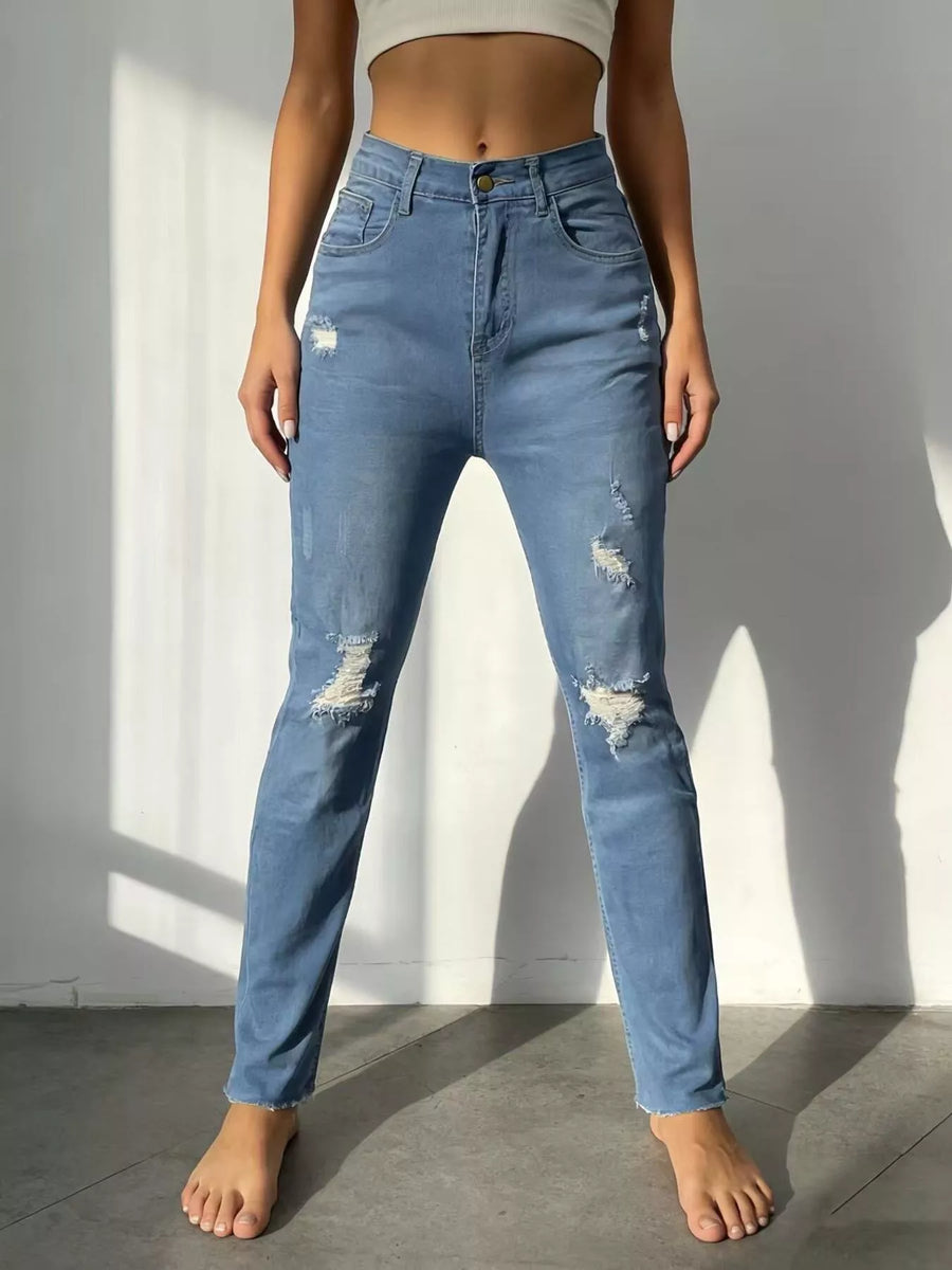 Person wearing blue distressed jeans standing against a plain wall.