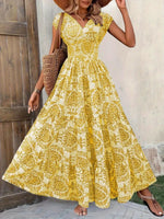 Woman wearing a yellow floral dress standing against a wooden door.