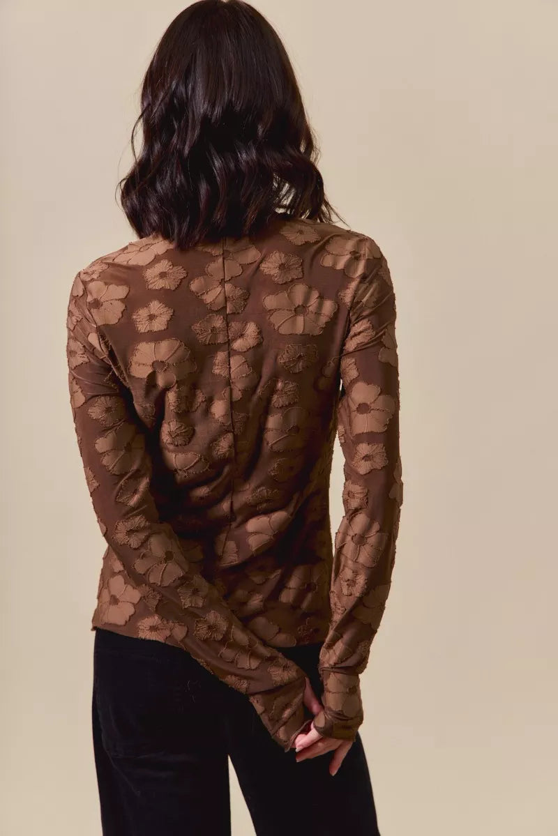 Person wearing a brown floral long-sleeve top against a beige background