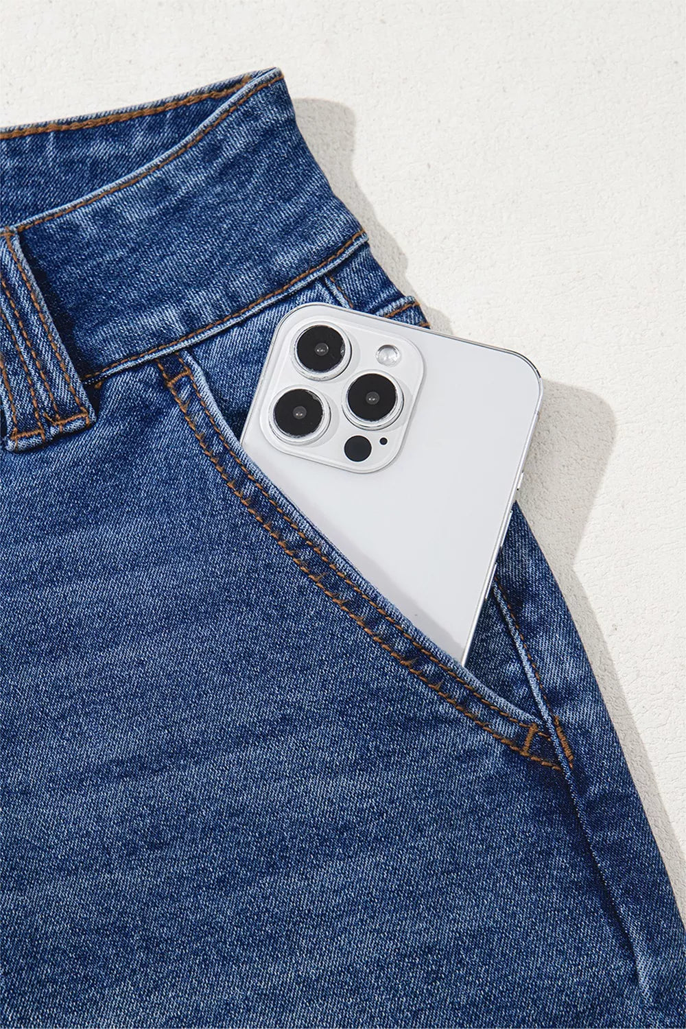 Smartphone with a white case in the pocket of blue jeans on a light gray background