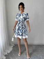 Woman wearing a blue floral dress with white accents in a minimalistic setting.