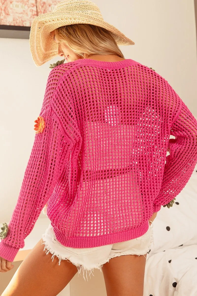 Person wearing a bright pink crochet cardigan with a straw hat and white shorts.