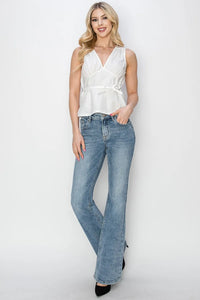 Woman wearing a white sleeveless top and blue jeans against a white background