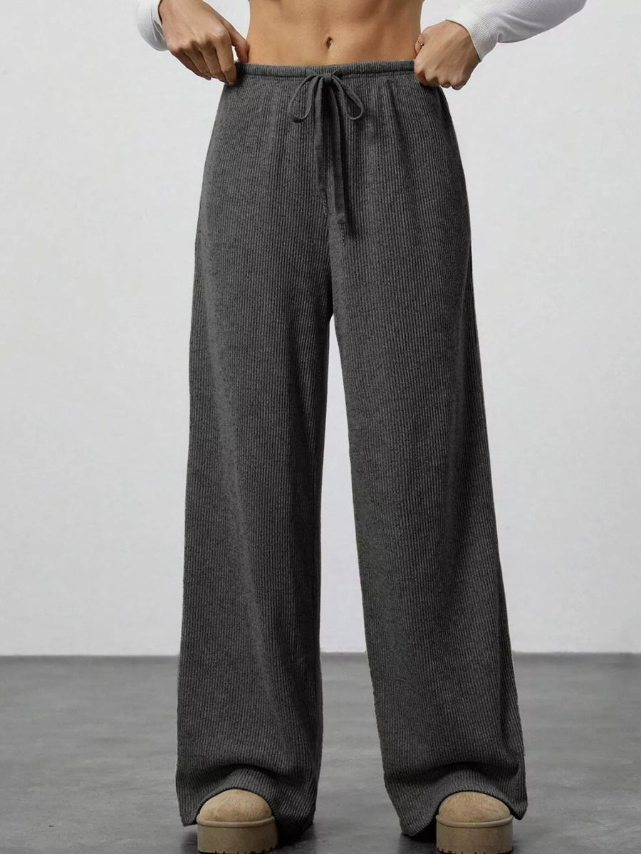 Person wearing gray wide-leg pants with a plain background