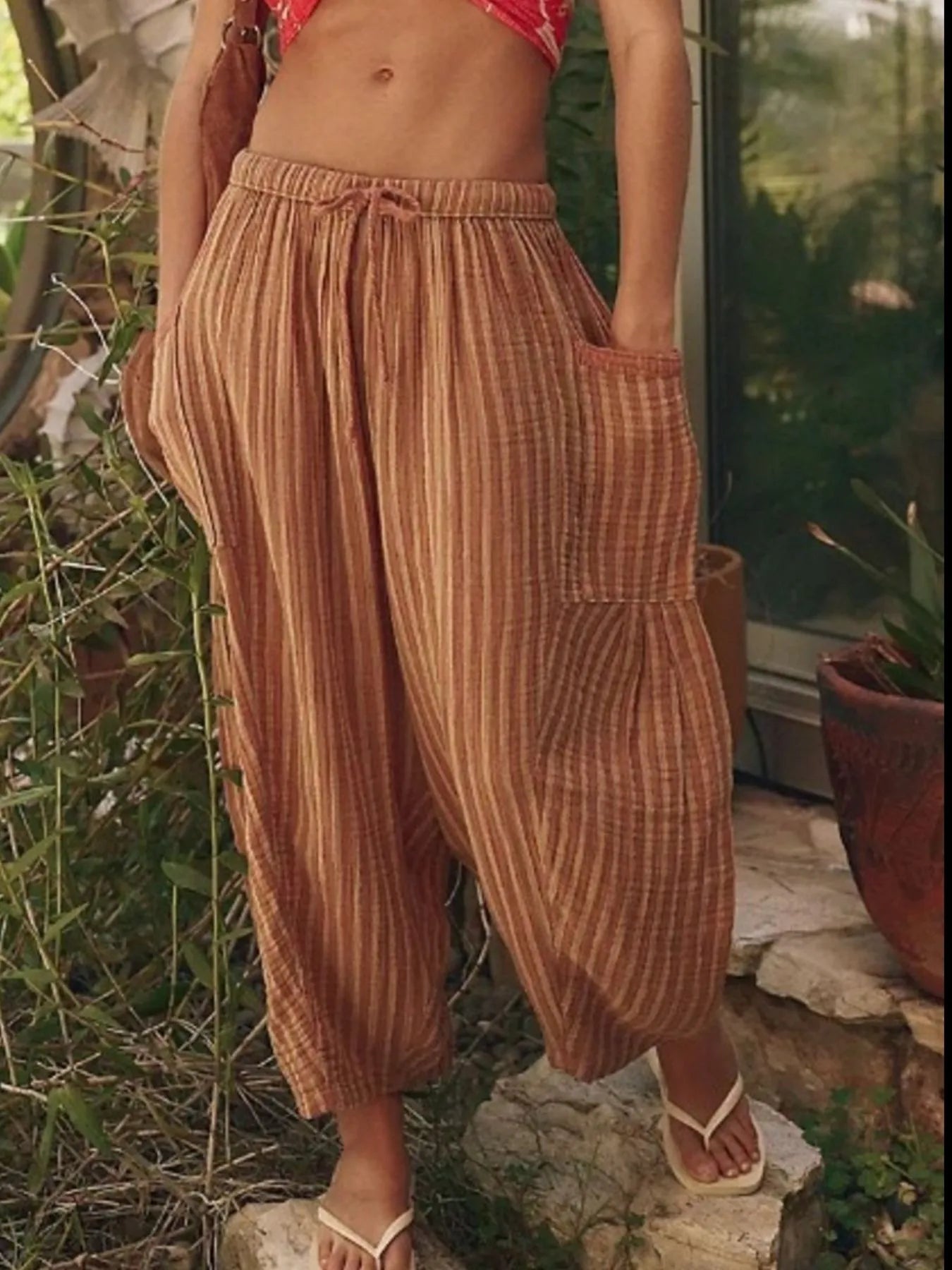 Person wearing brown striped pants standing outdoors with plants in the background