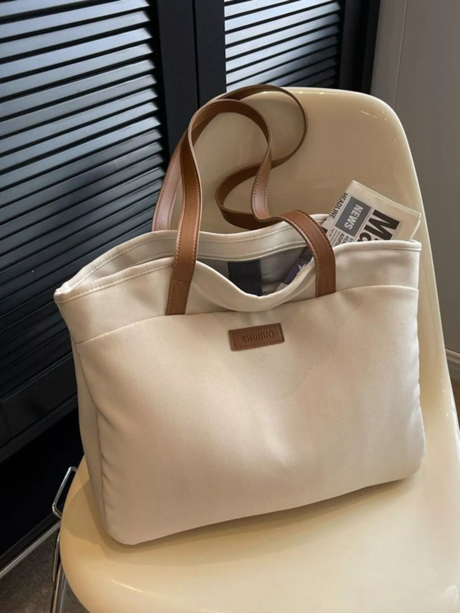 Beige tote bag with brown handles on a chair next to a window