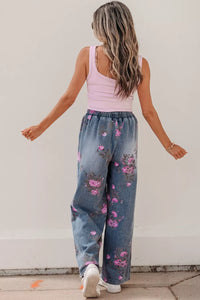 Woman wearing a pink tank top and floral jeans against a plain background