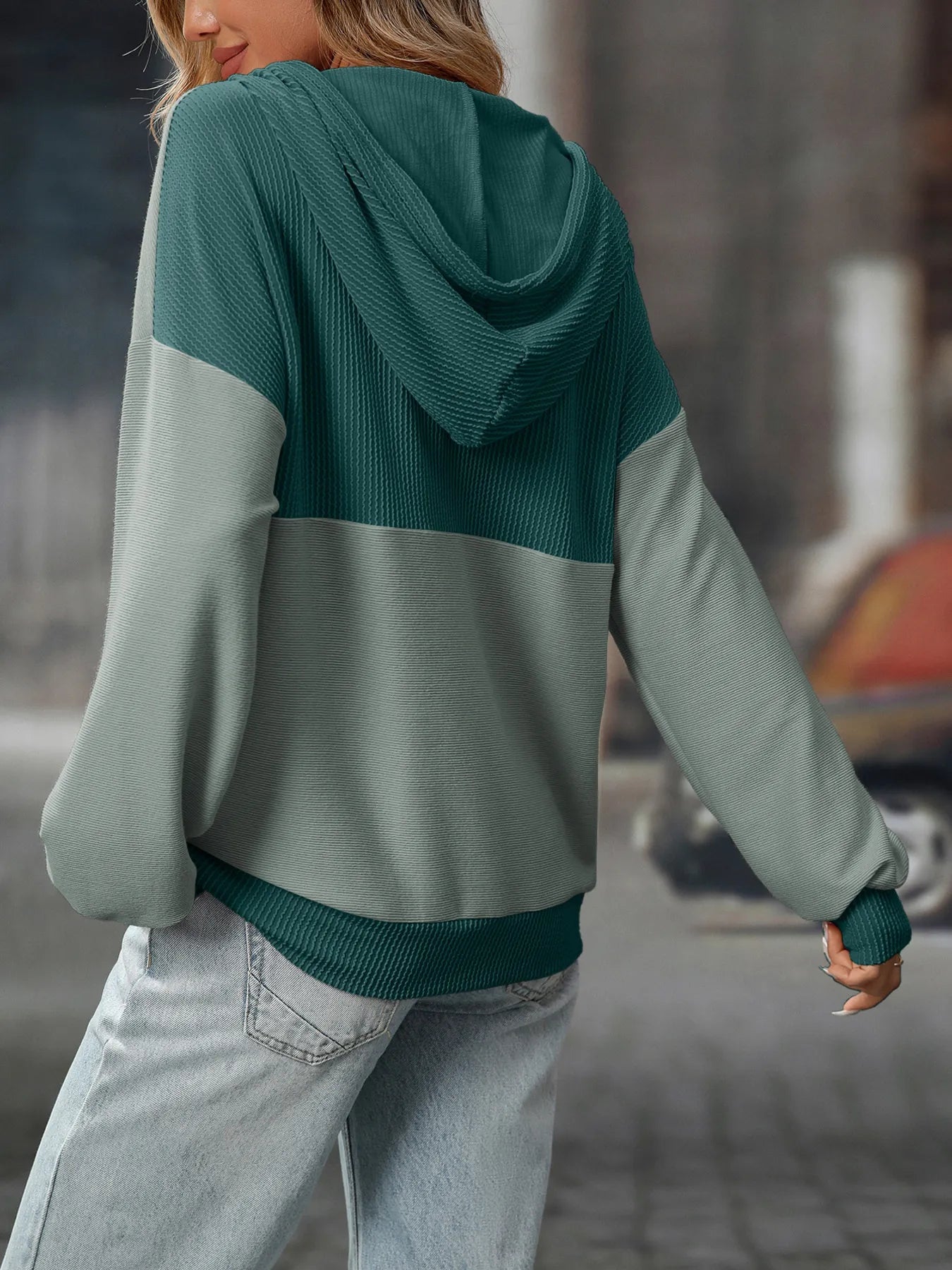 Person wearing a green and gray color-blocked hoodie in an urban setting