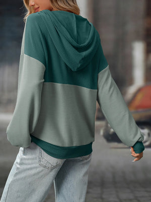 Person wearing a green and gray color-blocked hoodie in an urban setting