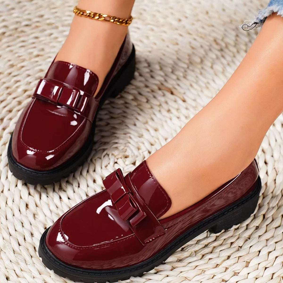 Burgundy loafers worn on a textured beige surface