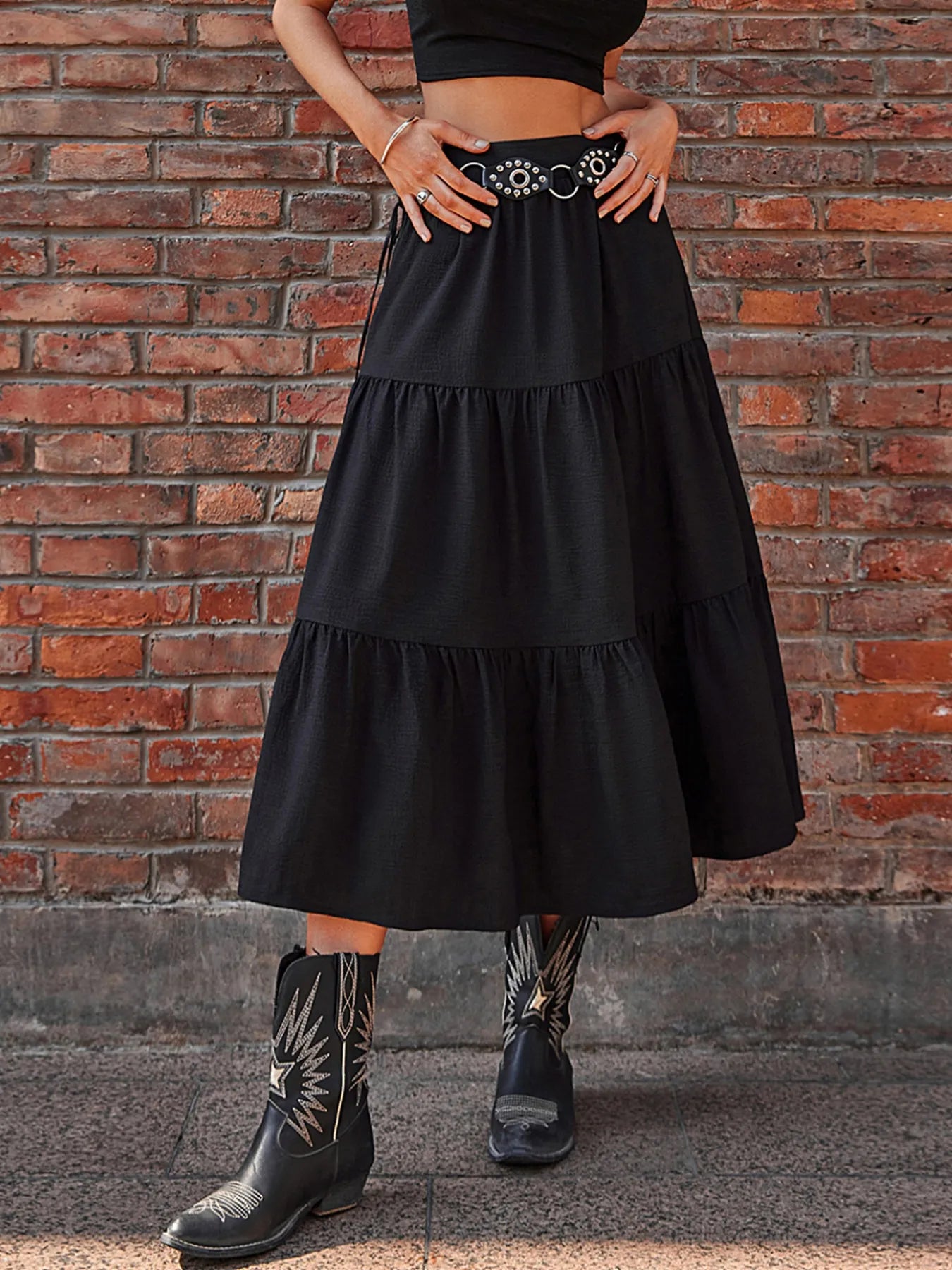 Person wearing a black tiered skirt and cowboy boots against a brick wall.