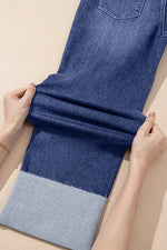 Person folding a blue denim fabric on a beige surface