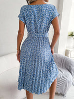 Woman wearing a blue floral dress in a room with a white couch and striped blanket.