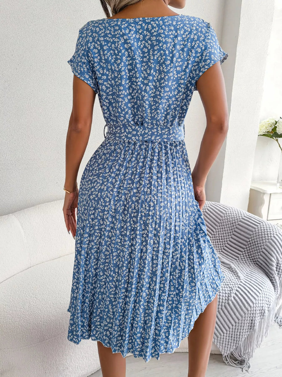Woman wearing a blue floral dress in a room with a white couch and striped blanket.