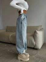 Person wearing light blue jeans and white sneakers in a room with a beige sofa.