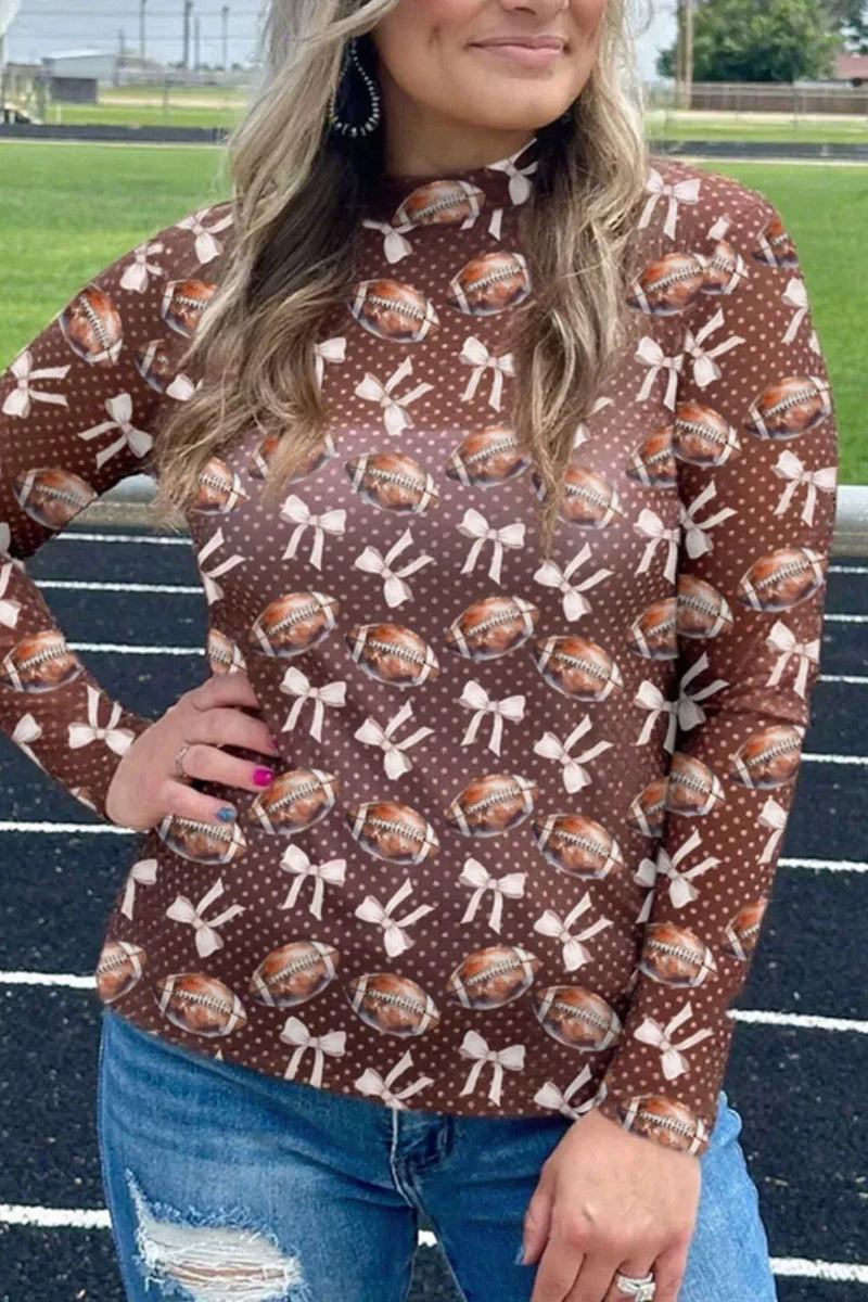 Person wearing a brown sweater with football and bow pattern on a sports field.