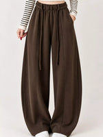 A person wearing loose, wide-leg brown pants with a drawstring waistband, paired with a black-and-white striped long-sleeve top, shown against a plain light background.