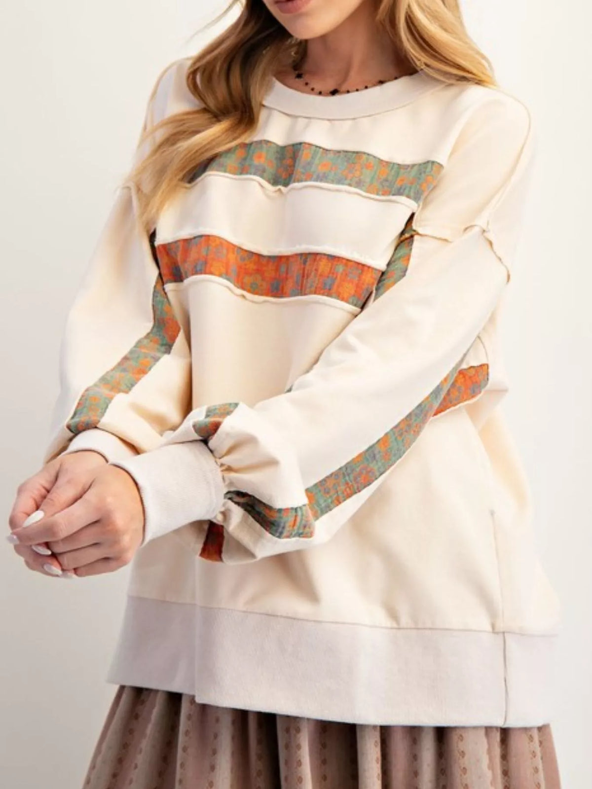 Person wearing a cream-colored sweatshirt with patterned sleeves on a plain background