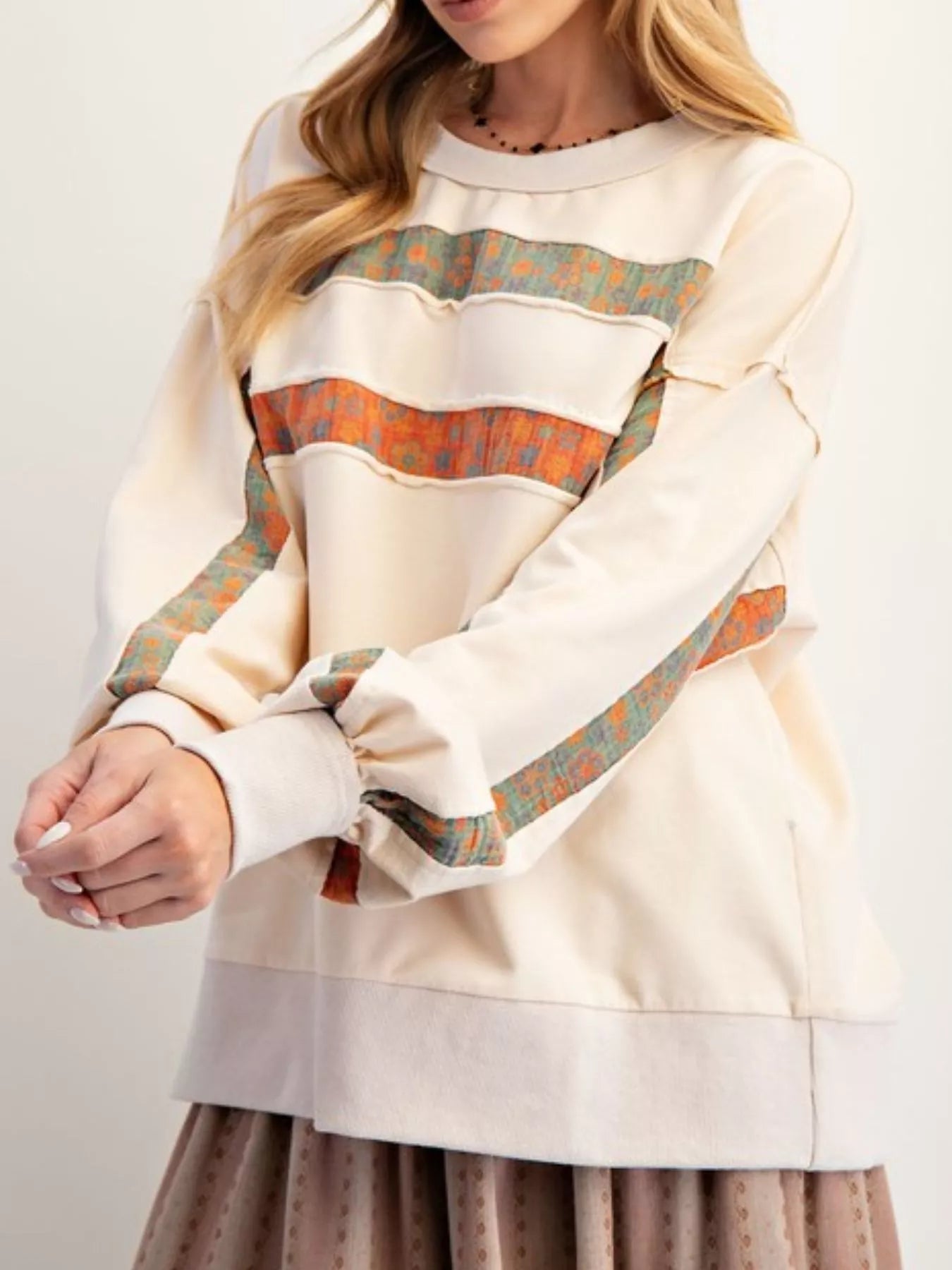 Person wearing a cream-colored sweatshirt with patterned sleeves on a plain background